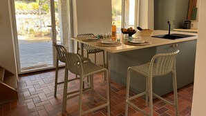 Een keuken met een centraal eiland, twee barkrukken, een spoelbak en een raam met uitzicht op een tuin.