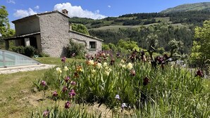 Een stenen huis met een tuin vol verschillende bloemen en uitzicht op glooiende heuvels.
