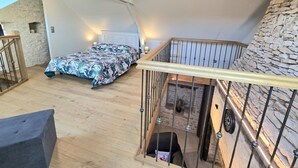 A bedroom with a bed, a staircase, and a stone wall. - Cozy house for couple with private spa in Périgord (Les Coteaux Périgourdins)