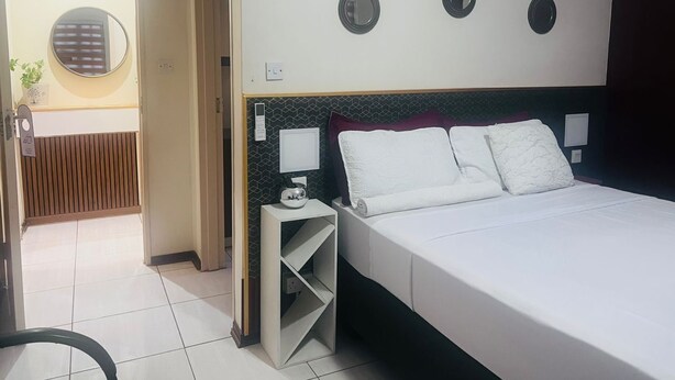 Ein Hotelzimmer mit einem großen Bett, einem Nachttisch mit Lampe, einem wandmontierten Spiegel und einer kleinen Ablage.