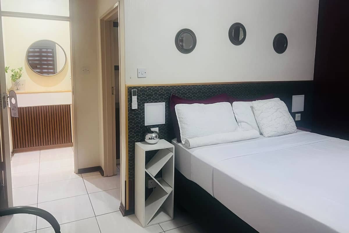 A hotel room with a large bed, a bedside table with a lamp, a wall-mounted mirror, and a small shelf.