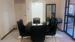 Ein Essbereich mit einem runden Tisch, schwarzen Stühlen mit goldfarbenen Beinen und einer Blumenvase.