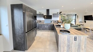 A modern kitchen with dark cabinetry, a stainless steel refrigerator, and a wooden island with a sink. - Large Family House with Private Pool and Pets Welcome (Coubjours)