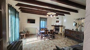 A spacious living room with a fireplace, wooden beams, a dining area, and a sofa. - Comfortable Country House in Dordogne (Saint-Rabier)