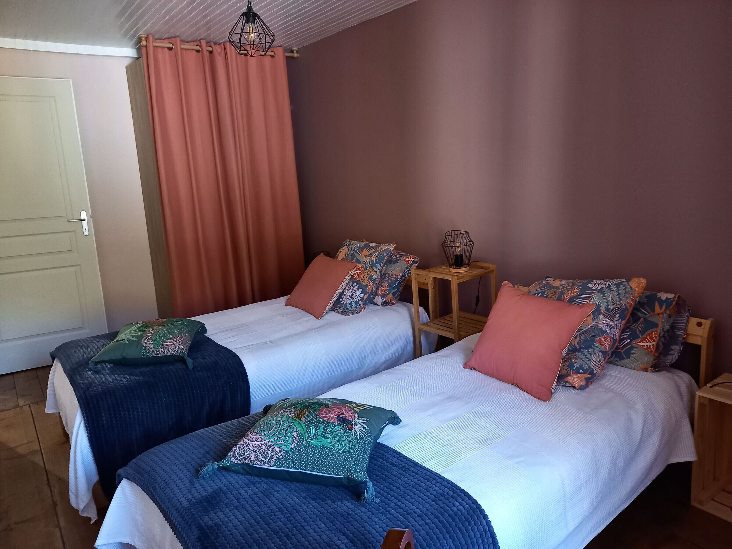 Ein Zimmer mit zwei Betten, jeweils mit gemusterten Kissen und einem Nachttisch mit Lampe.