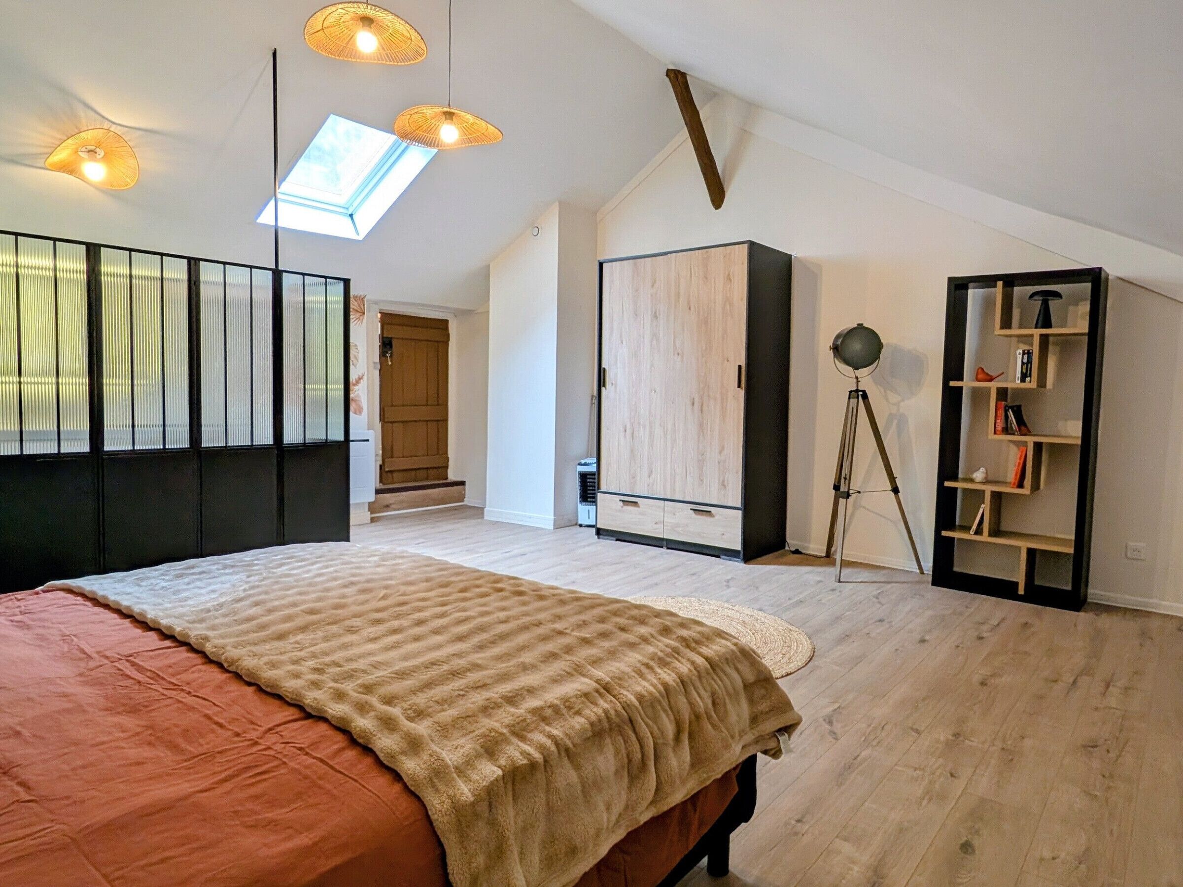 A bedroom with a large bed, a wardrobe, a tripod lamp, and a bookshelf.