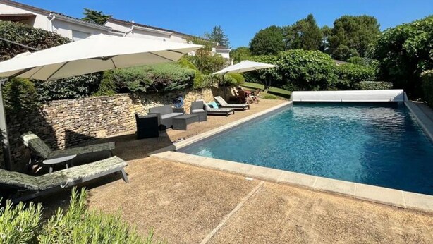 A swimming pool with lounge chairs and umbrellas, surrounded by a stone wall and greenery.