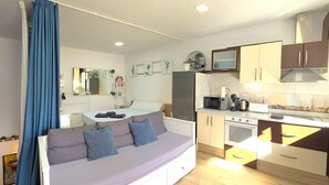 Un espacio habitable compacto con sofá cama, kitchenette y zona de comedor.