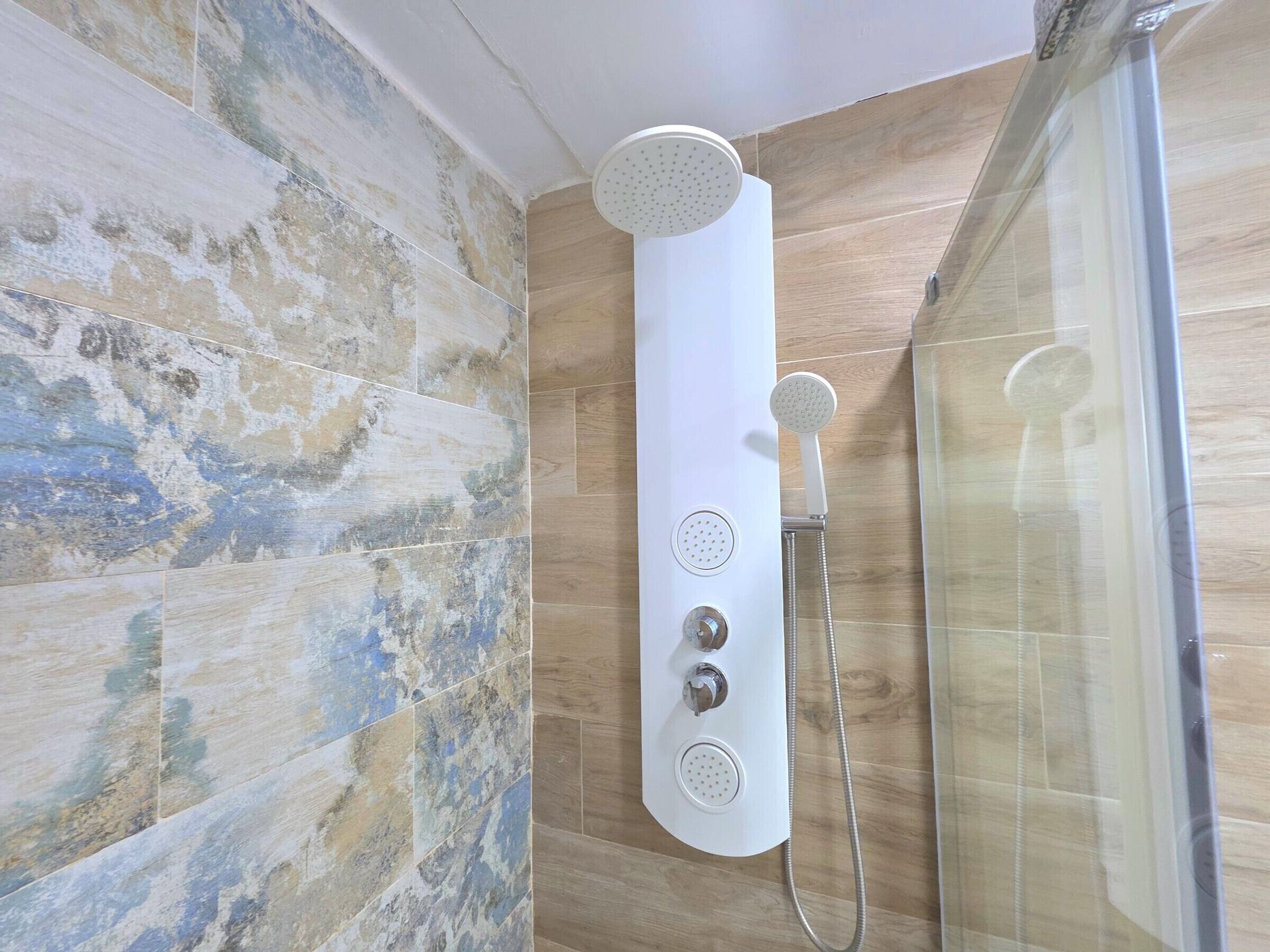 A modern shower with a handheld showerhead and a wall-mounted control panel.
