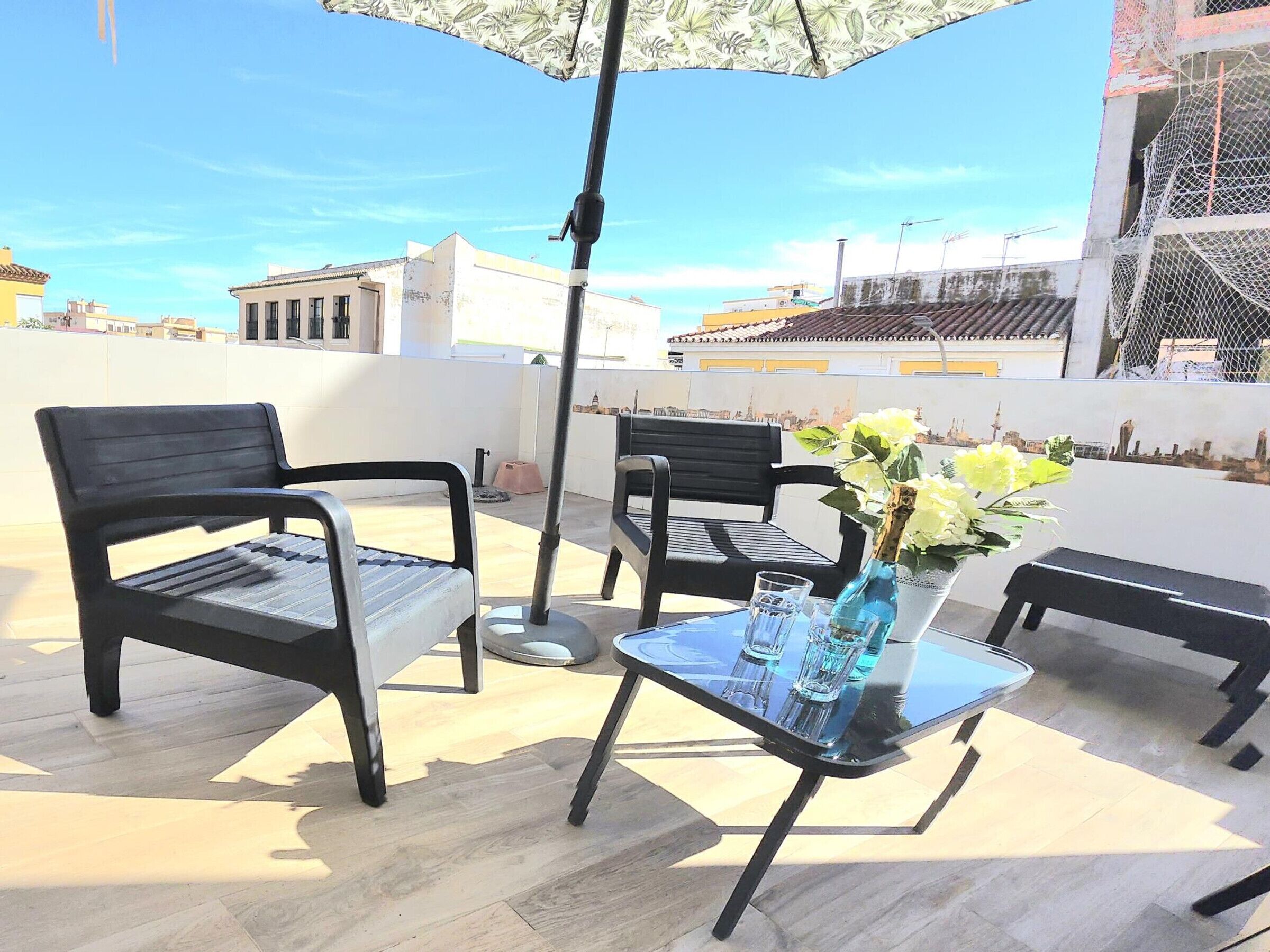 Eine Dachterrasse mit zwei schwarzen Stühlen, einem Glastisch und einer Vase mit Blumen.