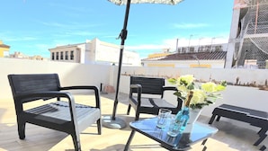 Una terraza en la azotea con dos sillas negras, una mesa de vidrio y un jarrón con flores.