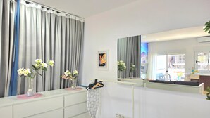 Un dormitorio con cama, cómoda, espejo y ventana con cortinas.