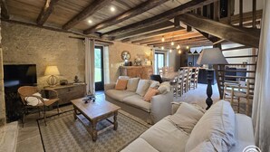 A rustic living room with exposed wooden beams, a sofa, a coffee table, and a television. - Stone house in Périgord, sleeps 10, authentic charm (La Chapelle-Aubareil)