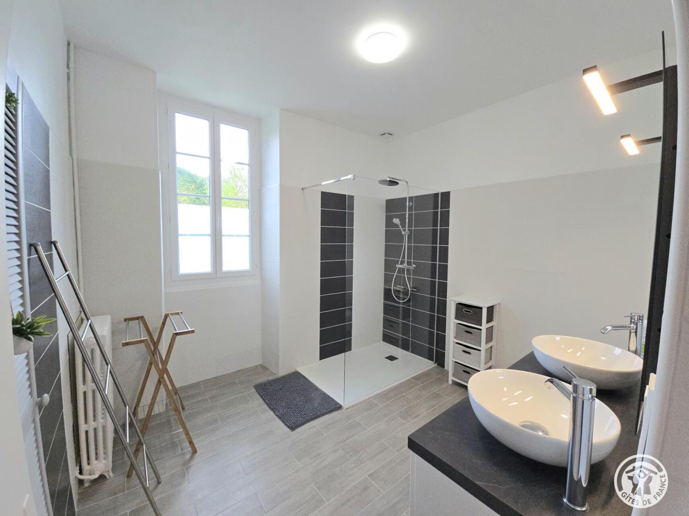 Une salle de bain moderne avec deux lavabos, une douche et une grande fenêtre.