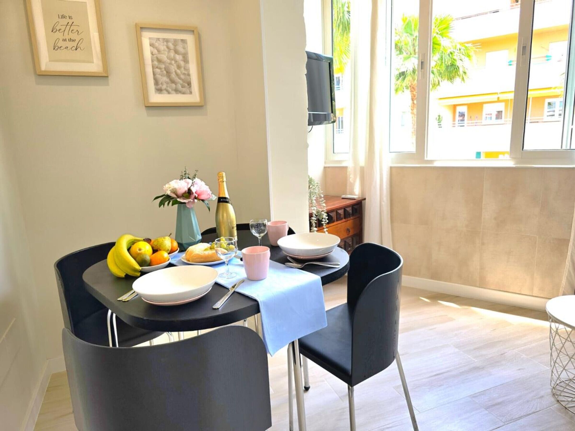 A dining area with a table set for two, featuring a bottle of champagne, fruit, and a vase of flowers.