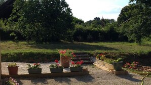 Ein Garten mit Kiesweg, Topfpflanzen und einer Holztreppe, die zu einer Rasenfläche führt.