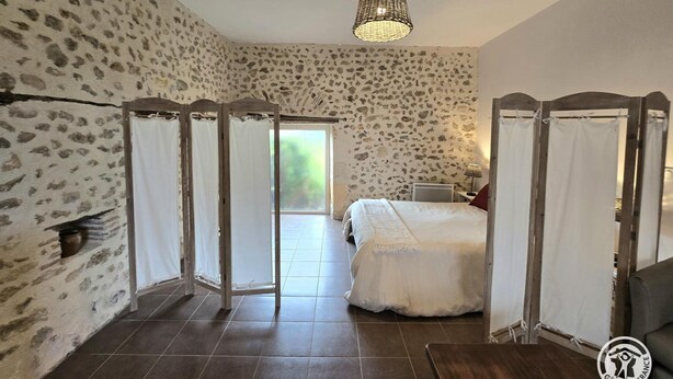 Ein Schlafzimmer mit Steinsandsteinwand, einem Himmelbett, einer Deckenleuchte und Blick durch eine Tür.