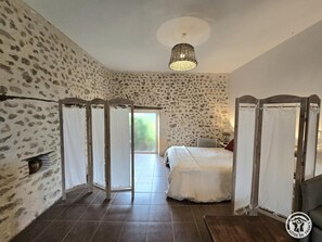 Un dormitorio con pared de piedra, cama con dosel, una lámpara en el techo y vistas a través de una puerta.