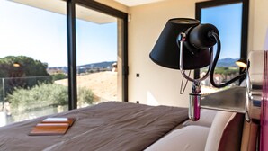 A bedroom with a large window, a bed with a pillow and a book, and a lamp on a bedside table.