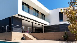 A modern two-story house with a swimming pool, large windows, and a minimalist design.