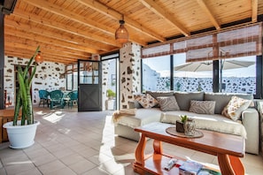 A spacious living area with a wooden ceiling, a sofa set, a coffee table, and a large window with a view of a rocky landscape.