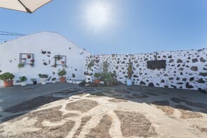 Ein Innenhof mit Blumentöpfen, einer weißen Wand mit Steinmuster und einem strahlend blauen Himmel.