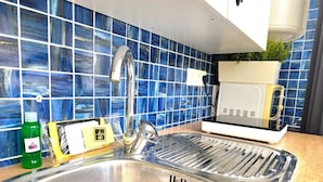 Uma cozinha com pia de aço inoxidável, backsplash com azulejos azuis, micro-ondas e uma garrafa verde de detergente.