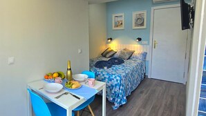 Quarto pequeno e compacto com cama, mesa de jantar e cadeiras, e uma área de cozinha compacta.