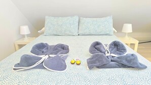Un lit avec une couvre-lit à motifs, deux serviettes et deux paires de chaussons.