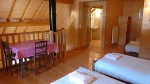 Une chambre avec deux lits, une table en bois recouverte d’une nappe à carreaux et une rambarde en bois.