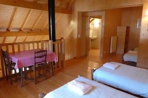 Ein Zimmer mit zwei Betten, einem Holztisch mit kariertem Tischläufer und einem Holzwandgeländer.