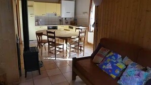 Un salon chaleureux avec un plancher en bois et un canapé agrémenté de coussins colorés. On aperçoit à l’arrière-plan un coin repas avec une table et des chaises en bois.