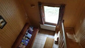 Une petite pièce avec un plancher en bois, une fenêtre avec des rideaux, un radiateur, un canapé avec des coussins et une petite table.