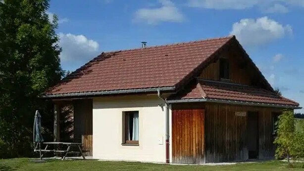 Une maison de plain-pied avec un toit recouvert de tuiles rouges, un petit porche et une porte en bois.