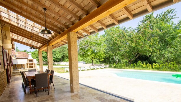 Eine Außenpatio mit Pool, Steinboden und einer Pergola.