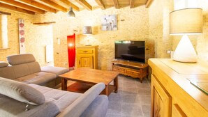 Ein gemütliches Wohnzimmer mit Sofa, Fernseher, Holzschrank und einer Lampe.