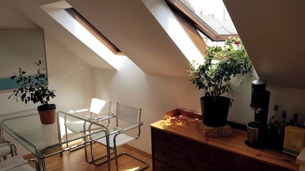 Een moderne loft slaapkamer met dakramen, een glazen eettafel en een houten dressoir.