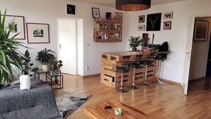 Een moderne woonkamer met een grijze bank, een houten salontafel en een keukenhoek met barkrukken.