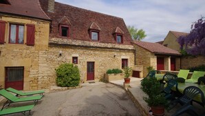Un edificio in pietra con un cortile interno, che include un piccolo giardino con piante in vaso e posti a sedere all'aperto.