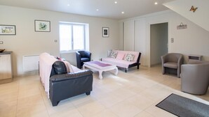 Ein geräumiges Wohnzimmer mit Sofa, Sessel und einem kleinen Tisch. Ein Fenster sorgt für natürliches Licht, und das Zimmer verfügt über eine hohe Decke mit Einbauleuchten.