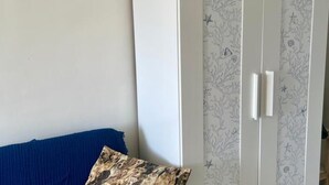 Una habitación con un sofá azul, un papel tapiz estampado y un armario blanco.
