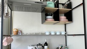 Cocina compacta con cafetera, hervidor y un bol de fruta en la encimera.