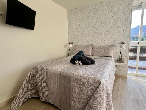 A bedroom with a patterned bedspread, a TV mounted on the wall, and a window with a view of mountains. - Modern Studio Benalmádena with Views (Marbella)