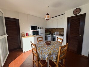 A compact kitchen with a dining table, chairs, a microwave, a television, and a clock on the wall. - Ground Floor T3 Quiet 200m Beach, Pets Ok, Parking (Le Barcarès)
