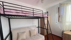 En våningssäng med en stege, en soffa och ett fönster med gardiner.