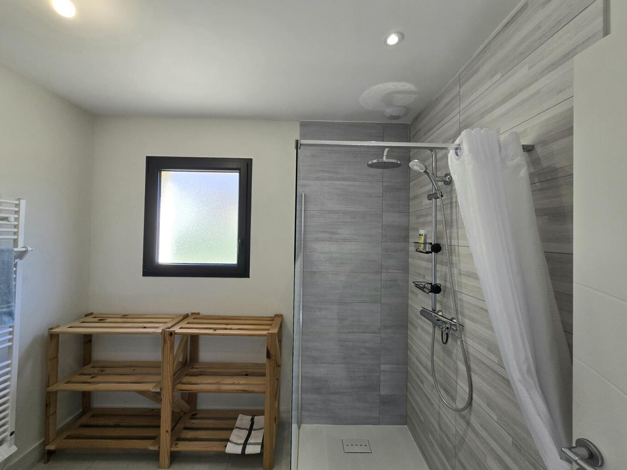 A modern bathroom with a shower, a window, and wooden shelves.