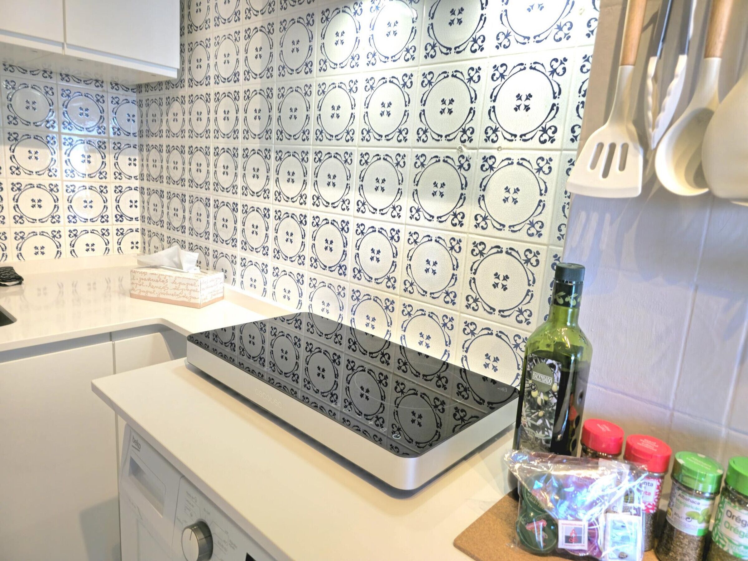 Een keuken met betegelde spatwand, een inbouwoven en verschillende keukengerei en specerijen op het aanrecht.