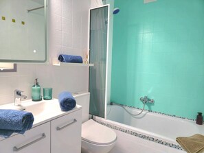 Une salle de bain avec des toilettes blanches, un lavabo avec un miroir et une baignoire avec un rideau de douche.