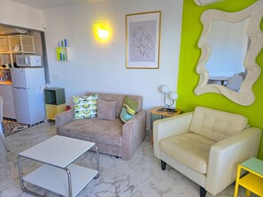 A living room with a sofa, a white armchair, a small table, and a kitchen area in the background. - Elegant urban retreat in Torremolinos with panoramic terraces (Torremolinos)