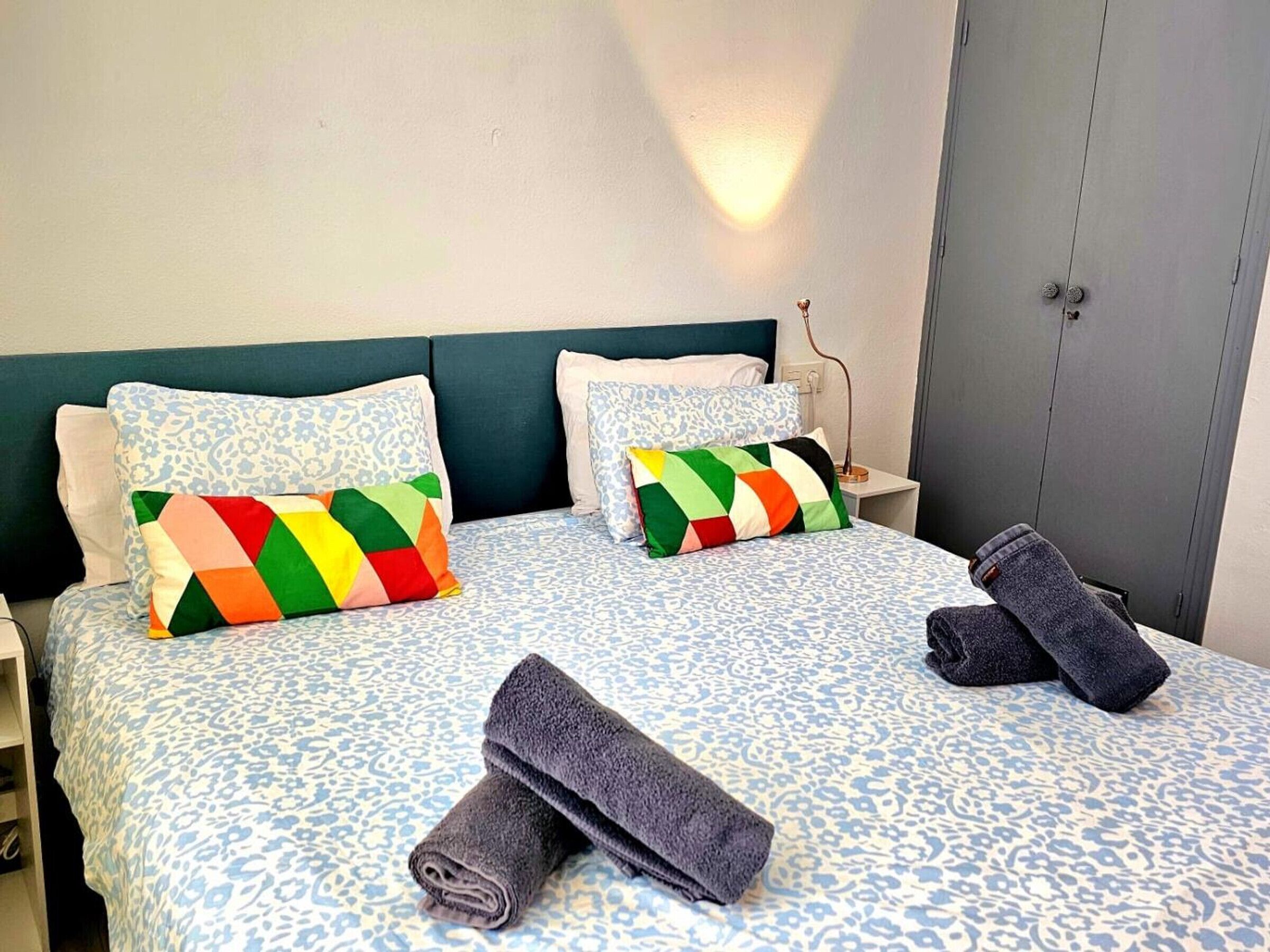 A hotel room with a bed, two pillows, a nightstand, a lamp, and a wardrobe.